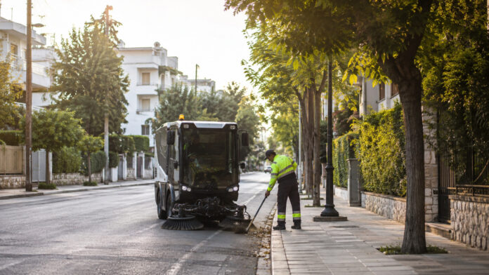 Δημοτικό σάρωθρο και εργαζόμενος καθαριότητας σε δενδροφυτεμένο δρόμο