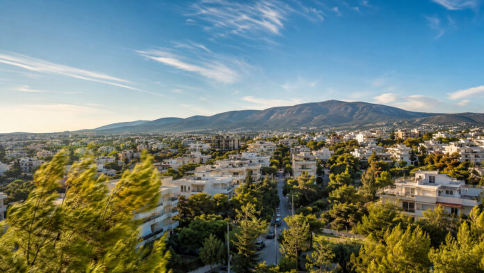 Ηλιόλουστη καλοκαιρινή εικόνα των βορείων προαστίων με δέντρα να κινούνται στον βοριά και την Πεντέλη στο βάθος