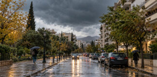 Αττική: Ισχυρές βροχές και καταιγίδες την Τρίτη 13 Οκτωβρίου Βροχερός δρόμος σε αστική γειτονιά της Αττικής με πεζούς που κρατούν ομπρέλες